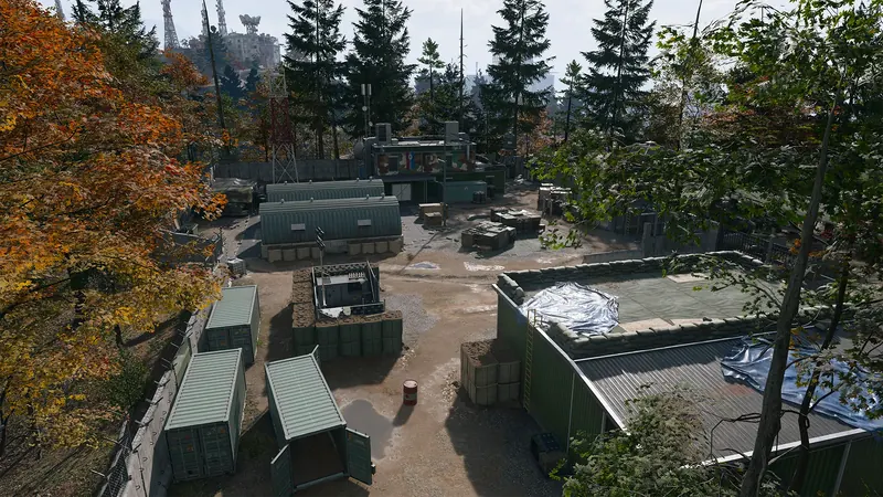 An overhead view of a forested military compound with storage containers, barracks, equipment, and defensive barriers.