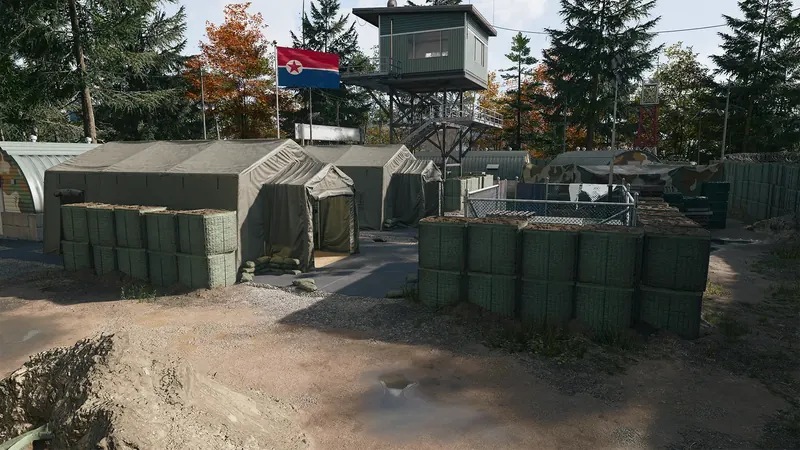 Military tents surrounded by defensive barriers sit beneath a guard tower flying a North Korean flag.