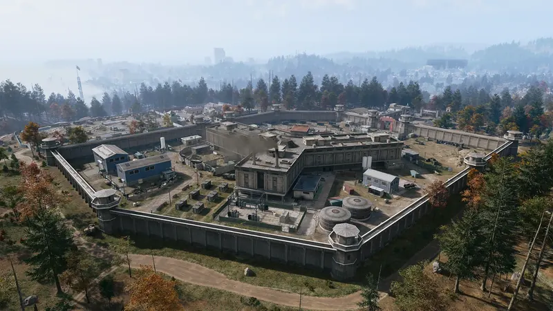 Aerial view of a large prison complex enclosed by concrete walls and guard towers, surrounded by dense forest.